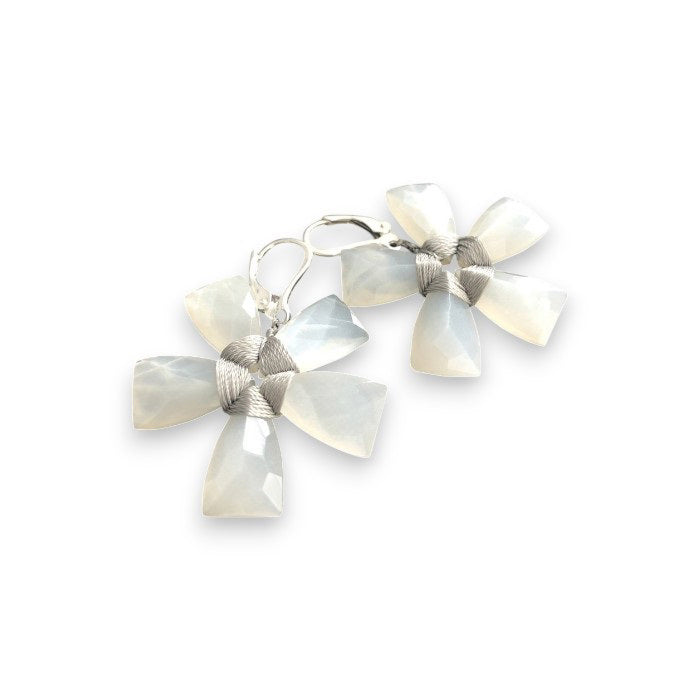The ANN LIGHTFOOT - WHITE MOONSTONE FLOWER EARRINGS by ANN LIGHTFOOT are displayed on a dark wooden surface, showcasing their exquisite design with moonstones forming petal-like shapes and accented with metallic wire at the center.