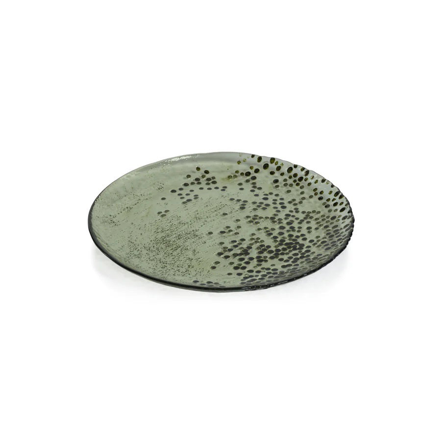 The DOTTED GLASS PLATE 8.25" by ZODAX is a round, shallow green plate with a textured surface and small, dark speckles on one side, perfect for serving and shown against a plain white background.