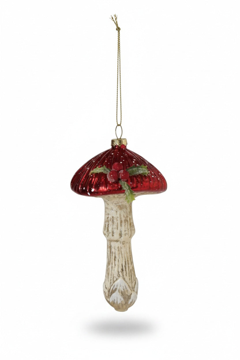 A MUSHROOM ORNAMENT WITH HOLLY AND GLITTER shaped like a glass mushroom with a shiny red cap, a textured off-white stem, and a small sprig of holly on top.
