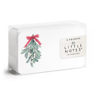 A clear plastic box contains 85 MISTLETOE LITTLE NOTES by E.FRANCES PAPER. The featured card displays a watercolor illustration of mistletoe with green leaves and white berries, beautifully tied with a pink bow. The label states "E. Frances, 85 MISTLETOE LITTLE NOTES, use unsparingly.