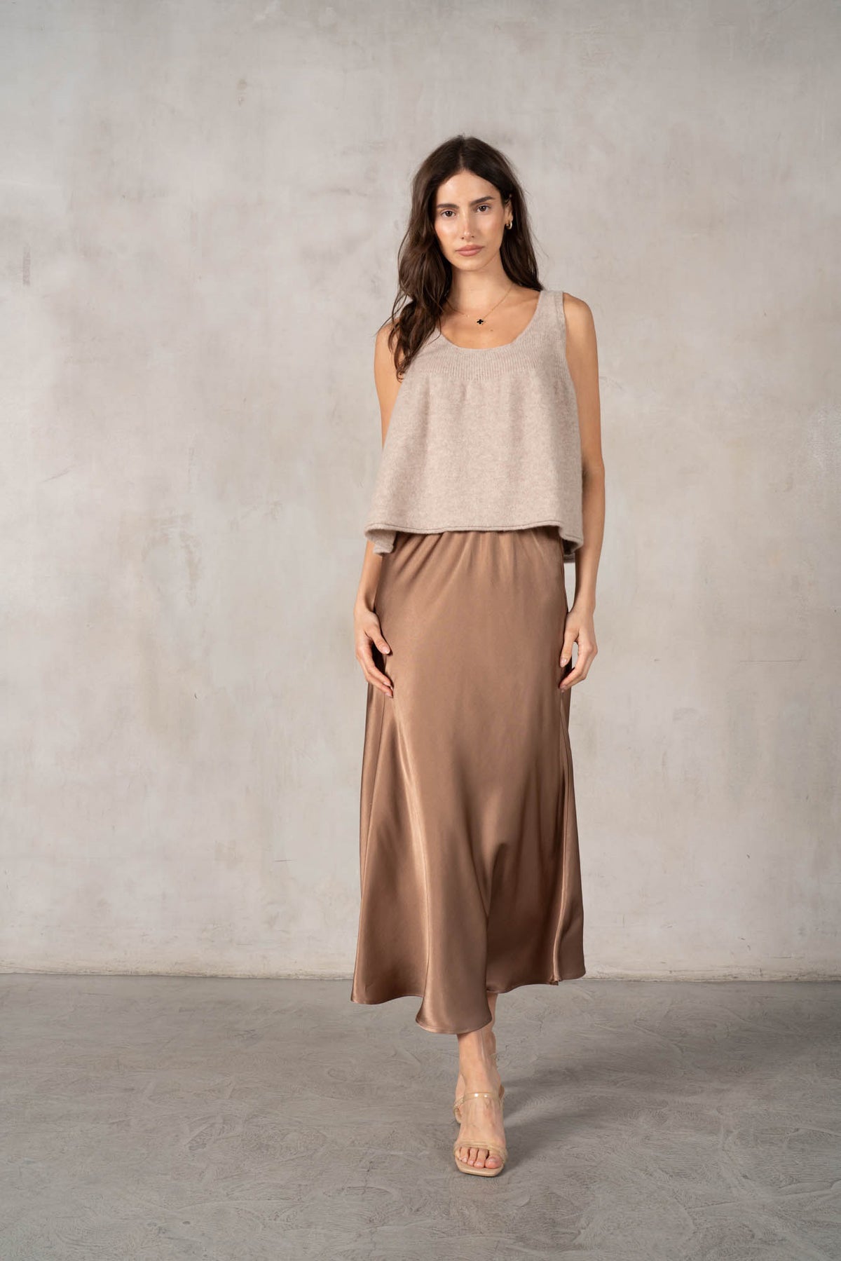 An older woman with long gray hair stands smiling in a dark red ROSE &amp; CROWN cardigan, the ROSE AND CROWN - SATIN MIDI SKIRT, and black knee-high boots against a plain white background.