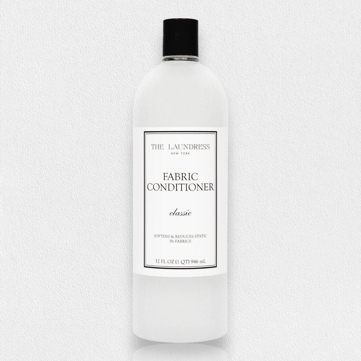 A white bottle of THE LAUNDRESS - FABRIC CONDITIONER 32OZ with a &quot;Classic&quot; scent label. This 32 fluid ounce (946 milliliters) fabric conditioner by THE LAUNDRESS promises to soften fabrics and reduce static. The bottle features a black cap, set against a light gray background.