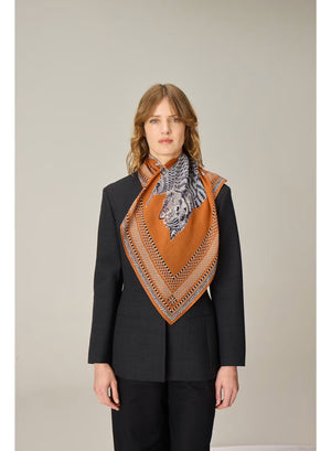 Showcasing a drawing of a striped cat and an intricately detailed owl perched side by side on a branch, set against a terracotta brown background with an ornate patterned border, the INOUI EDITIONS - CHOUETTE SQUARE MODAL SILK SCARF IN TERRACOTTA by INOUI is expertly crafted in India. Measuring 70 x 70 cm, this unique scarf features intricate details reminiscent of traditional artistry.