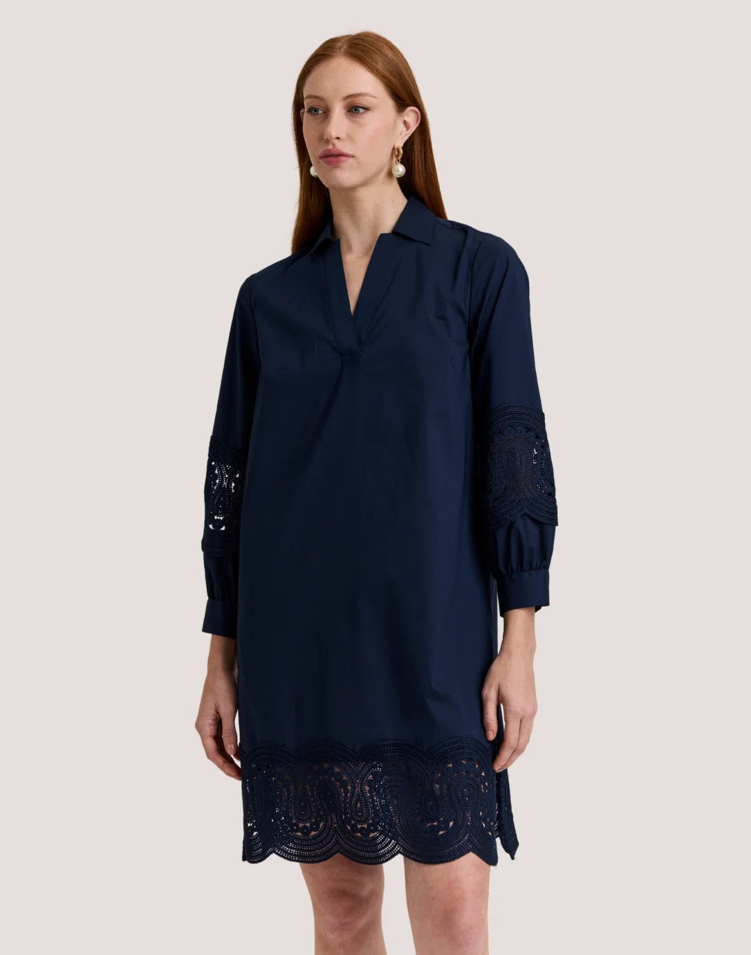 A woman with long red hair wears the HINSON WU Mona Bracelet Sleeve Lace Stretch Polished Cotton Dress in Navy. Crafted from stretch polished cotton, the dress features eyelet lace details on the sleeves and hem. She stands against a plain light background, looking slightly to the side with a neutral expression, her outfit highlighting its polished finish.