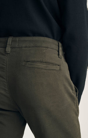 A person stands with their back to the camera against a neutral background, wearing the 34 HERITAGE - VERONA Straight Leg Chino Pant in Jasper High Flyer paired with a black long-sleeve shirt and brown suede shoes.