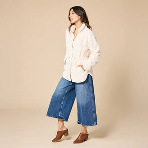 A woman wearing a cream SOFTIES - DREAMPLUSH DOUBLE ZIP JACKET / TUNIC with a cinched waist, paired with wide-leg denim culottes for cozy velvety softness.