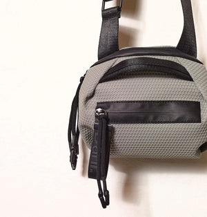 A person in a light beige suit carries the DANIELLA LEHAVI - BONNIE TRAVEL CROSSBODY, a large brown vegan bag with black zipper and strap, shown from shoulders to mid-thigh against a plain background.