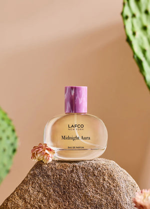 A LAFCO Fine Fragrance, Midnight Aura 50ml box rests on a rock, framed by flowers and green cactus pads in the background, capturing the essence of this alluring fruity perfume crafted with essential oils.