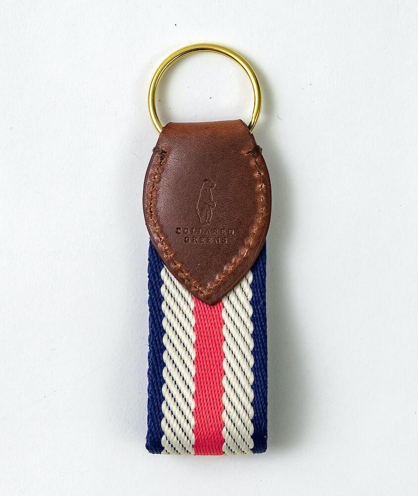 The COLLARED GREENS Dockside Key Chain in Coral White Navy by BIRD DOG BAY features a gold key ring, embossed leather top, and striped fabric strap. Proudly American Made and crafted with quality materials in the USA.