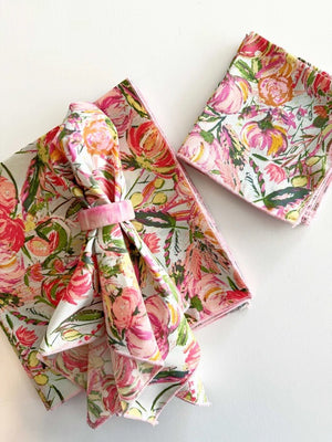 Three DOT AND ARMY FLORAL FROLIC DINNER NAPKINS in pastel pink, green, and yellow floral patterns are shown on a white surface—super soft, one is folded with a fabric napkin ring while two are stacked.