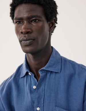 A person with short, curly black hair is seen from behind wearing the HARTFORD - PAUL Linen Shirt in Denim by HARTFORD, set against a plain light background.