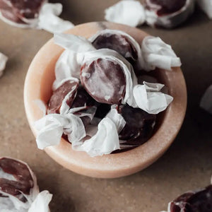 A rectangular box of JACOBSEN SALT CO. CHOCOLATE CARAMELS WITH SEA SALT stands on a light surface, featuring tan packaging with brown abstract patterns and a white label displaying the product name in black and gold.