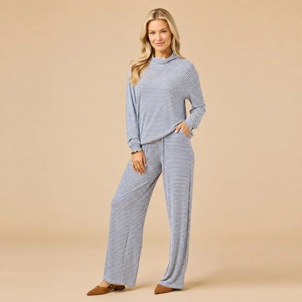 A woman wears a navy blue SOFTIES - DREAM JERSEY COWL NECK LOUNGE SET consisting of a long-sleeved top and wide-leg trousers.
