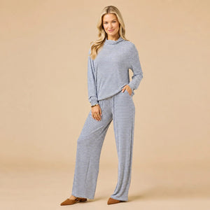 A woman wears a navy blue SOFTIES - DREAM JERSEY COWL NECK LOUNGE SET consisting of a long-sleeved top and wide-leg trousers.