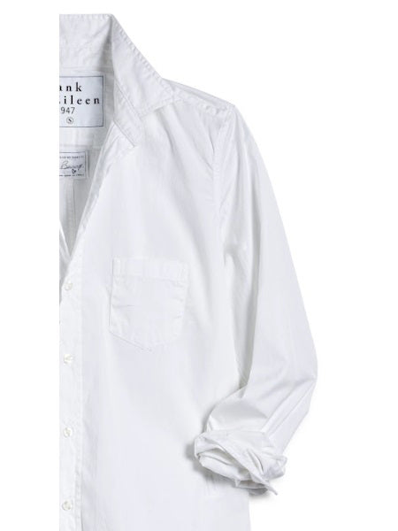 A man with short curly hair wears the FRANK &amp; EILEEN LUKE Men's Button Up Shirt in Classic White Poplin (sleeves rolled), paired with light blue ripped jeans and a watch, smiling slightly against a plain background.