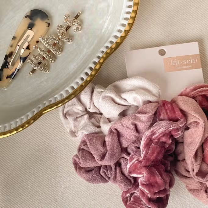 The KITSCH Velvet Scrunchies, perfect hair accessories in dusty pink and sage green, boast a soft texture. They come elegantly gathered on a white card labeled "KITSCH" with "SCRUNCHIE" below.