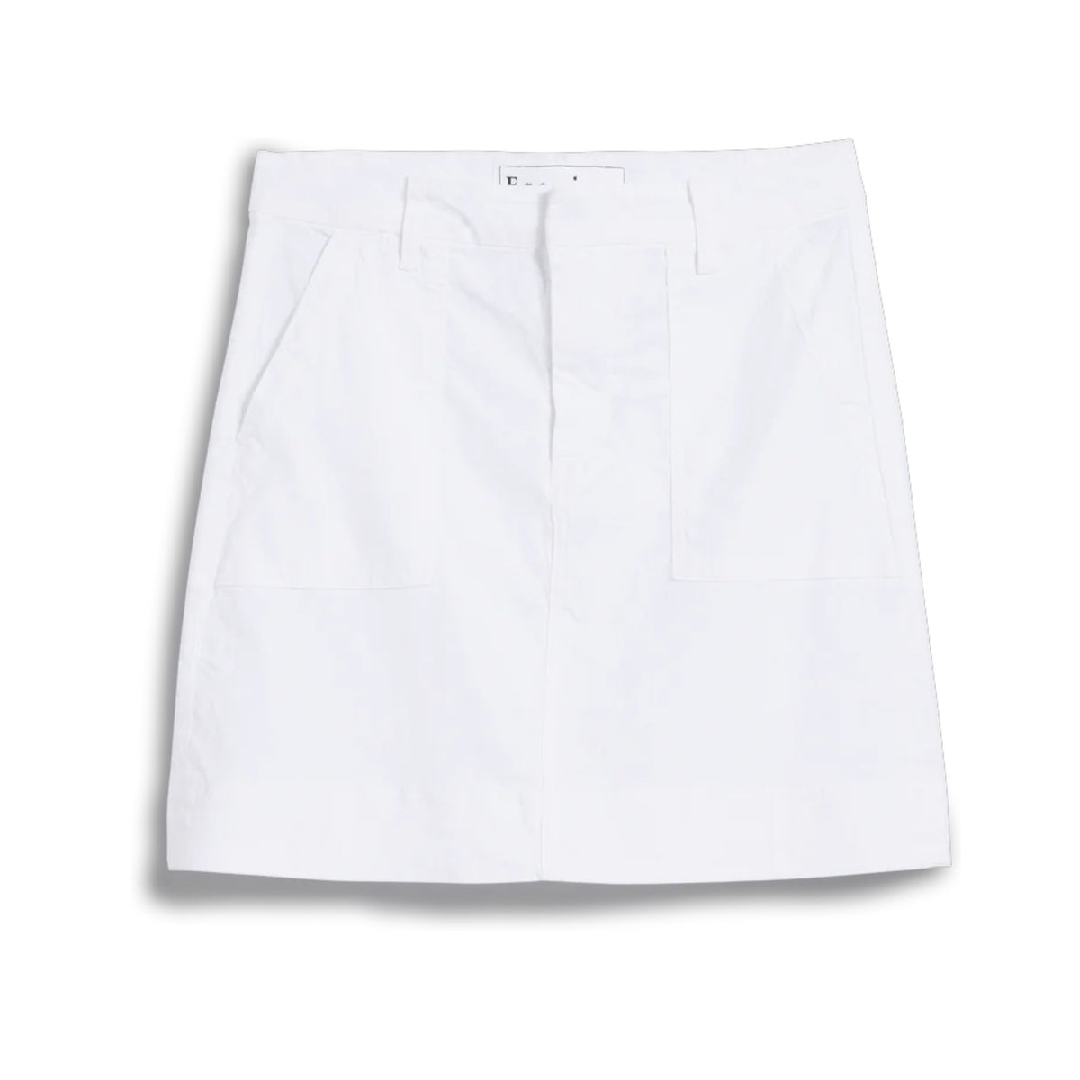 A person stands outdoors with one hand in the utility pocket of the FRANK &amp; EILEEN Jameson Utility Skirt in Performance Linen White, paired with a long-sleeve black-and-white striped shirt. Greenery and sunlight fill the background.