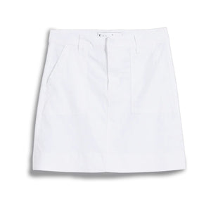 A person stands outdoors with one hand in the utility pocket of the FRANK & EILEEN Jameson Utility Skirt in Performance Linen White, paired with a long-sleeve black-and-white striped shirt. Greenery and sunlight fill the background.