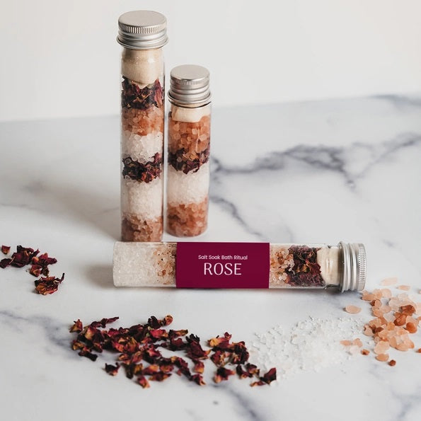 A transparent test tube filled with pink and white salt crystals and sealed with a silver metal cap, this BOTANICAL BATH SALT TUBE - ROSE by GIFTEN MARKET features a maroon label printed with “ROSE.” Ideal for an indulgent botanical soak, these rose bath salts gently fragrance your bath while nourishing your skin with calming minerals.