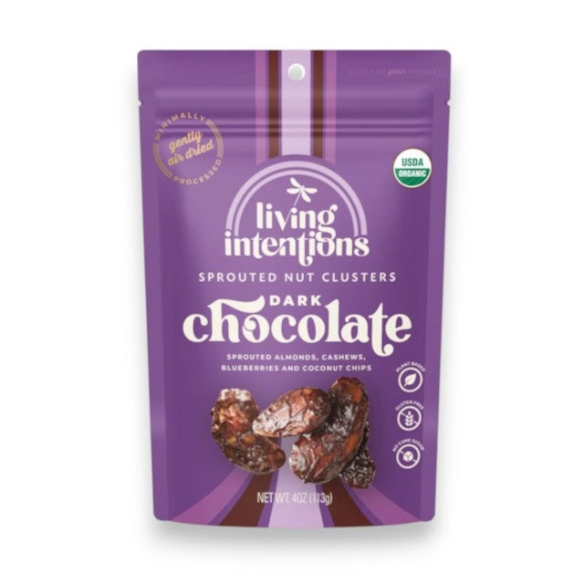 A beige bag of LIVING INTENTIONS DARK CHOCOLATE SPROUTED NUT CLUSTERS showcases vibrant images of nuts, cacao pieces, and blueberries on the packaging. The package prominently features labels for organic, paleo-friendly, gluten-free, and USDA Organic certifications.