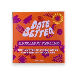 The "DATE BETTER - HAZELNUT PRALINE COVERED DATES" from DATE BETTER SNACKS features orange packaging with bold pink and purple text, adorned with abstract flower and leaf patterns. This 85% dark chocolate Medjool date treat weighs 1.8 oz.
