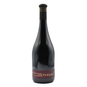 A dark glass wine bottle with a long neck and a black capsule on top features a black and maroon label reading “TURLEY.” Crafted by WINE: ADVINTAGE, this distinctive bottle contains their TURLEY ‘DEL BARBA’ ZINFANDEL 2023, renowned for its rich character and celebrated old vine heritage.