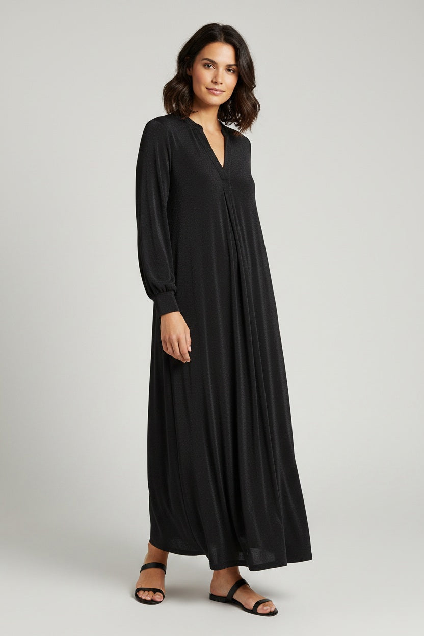 A woman wearing the MOMONI - AMEDE DRESS IN LUREX JERSEY and a black wide-brimmed hat stands in an ornately decorated room with large mirrors and intricate wall designs.