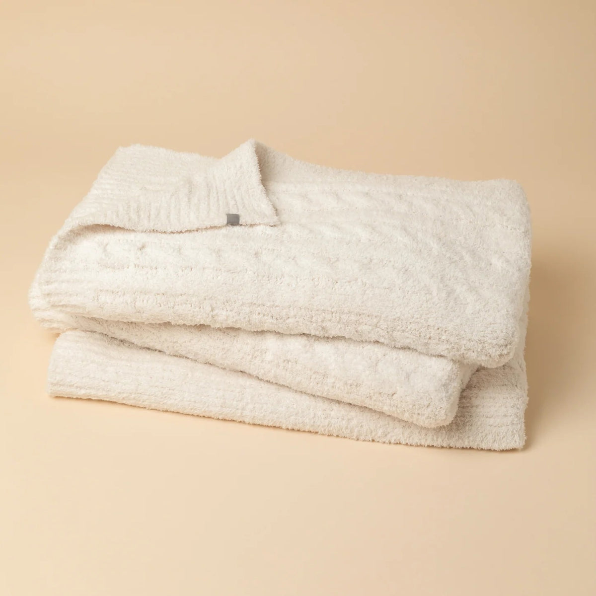 Folded off-white SOFTIES - CABLE KNIT MARSHMALLOW BLANKET tied with a branded ribbon.