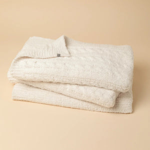 Folded off-white SOFTIES - CABLE KNIT MARSHMALLOW BLANKET tied with a branded ribbon.