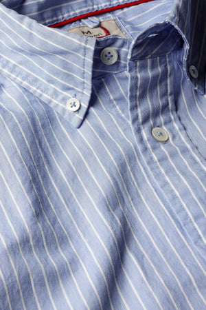 A close-up of the RELWEN - Dress Blues Shirt in Blue with White Stripe Twill by RELWEN, showcasing its light blue 100% cotton twill fabric with fine white stripes, white buttons, a classic collar, and detailed stitching that highlights the quality craftsmanship.