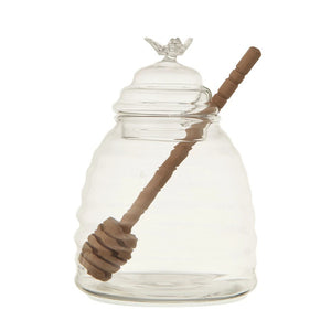 The CREATIVE COOP GLASS BEES NEST HONEY JAR is a beehive-shaped clear glass honey pot, featuring a lid topped with a small glass bee and comes with a wood honey dipper inside.