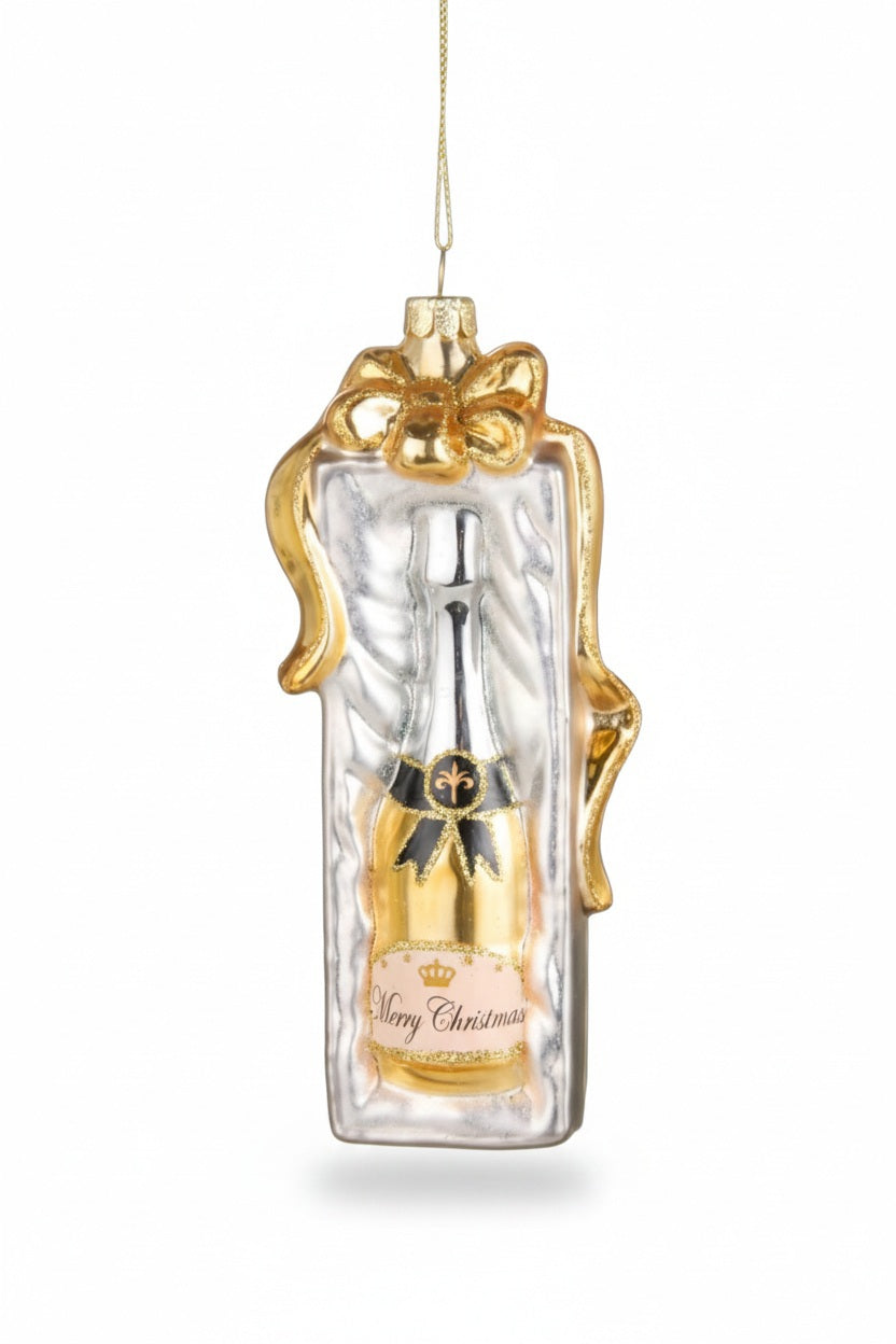 A RAZ IMPORTS CHAMAGNE GIFT ORNAMENT shaped like a champagne bottle gift box, wrapped in a gold ribbon with a label reading “Merry Christmas.”
