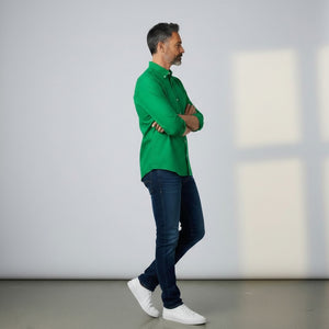 A man with short gray hair and a beard stands facing forward, wearing the FRANK & EILEEN LUKE Men's Button Up Shirt in Famous Denim Birdie with rolled-up sleeves and dark blue jeans against a plain light gray background.