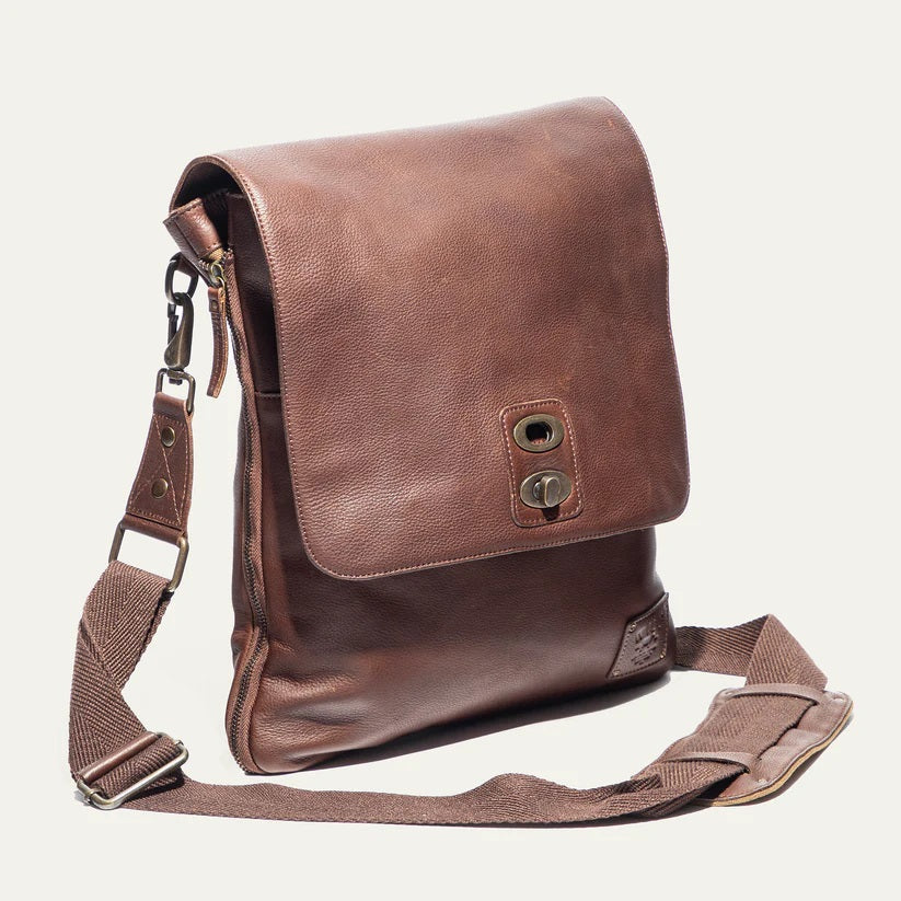 The WILL LEATHER GOODS - OTTO CROSSBODY BAG IN COGNAC, a full-grain leather bag with plaid lining, is shown open from above holding a camera, book, and wallet.