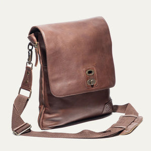 The WILL LEATHER GOODS - OTTO CROSSBODY BAG IN COGNAC, a full-grain leather bag with plaid lining, is shown open from above holding a camera, book, and wallet.