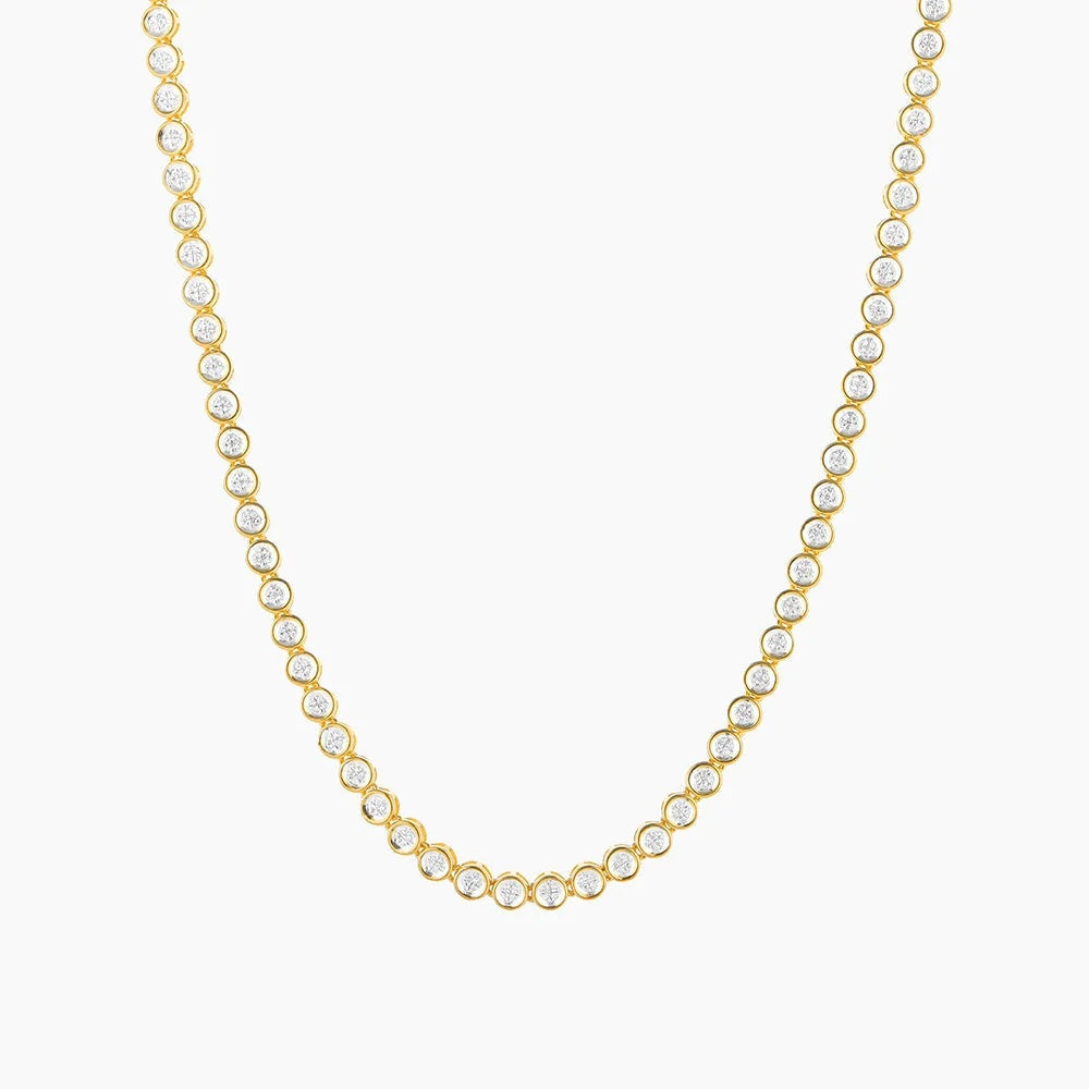 The ELLA STEIN - DIAMOND ESSENTIAL TENNIS NECKLACE by ELLA STEIN is a gold-plated piece adorned with a continuous row of evenly spaced round, white gemstones along the chain, beautifully displayed on a white background. This elegant necklace blends classic design with the lasting durability of stainless steel.