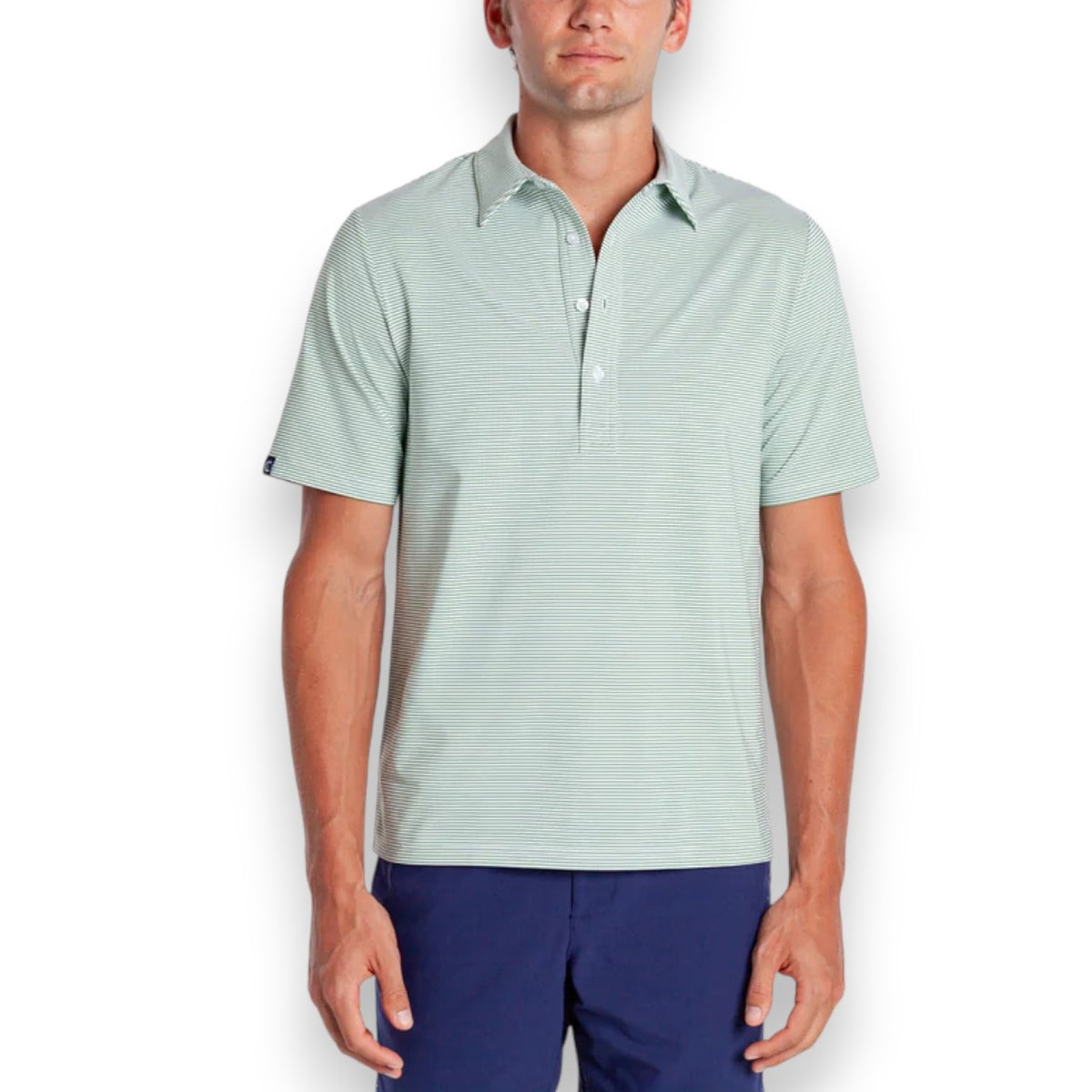 A man in a CRIQUET PERFORMANCE SPORT RANGE POLO IN HOBBY STRIPE - GATOR walks on a golf course, wearing blue pants, a white cap and glove, holding a club and smiling. Trees and a golf cart are visible in the background.