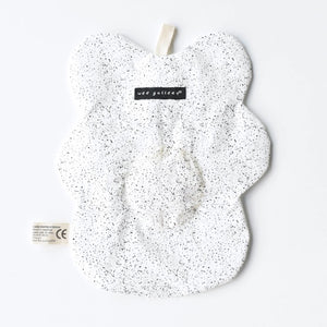 The WEE GALLERY - EGG CRINKLE TOY by WEE GALLERY is a white baby crinkle toy in the shape of a flower with a yellow circle at the center that features a smiling face with closed eyes. Made from organic cotton, it comes with a brown tag inscribed "Baby Crinkle Toy - Organic Crinkle Toy." The toy is displayed hanging on a white hook.