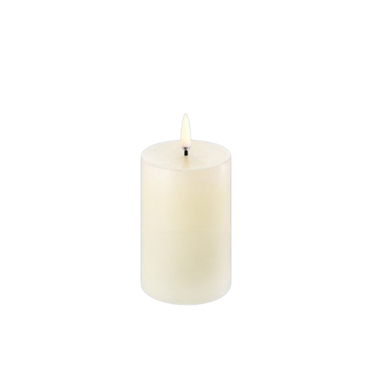 Three lit PIFFANY UYUNI Ivory Pillar Candles (2x3) are arranged on a wooden tray alongside ceramic decor and dishes atop a table. A small knife with a wooden handle rests nearby, while stacked bowls and a softly blurred sofa complete the minimal, cozy scene.