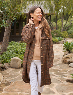 The Gavin Italian Boucle Shirt Jacket from Frank & Eileen is a long, plaid coat in shades of brown with an oversized fit. Made from luxurious pre-washed wool, the coat features a collared neckline, button closure, and two large front pockets. Sleeves are rolled to mid-length and the fabric showcases a textural, woven appearance. The tag inside reads "Frank & Ellen.