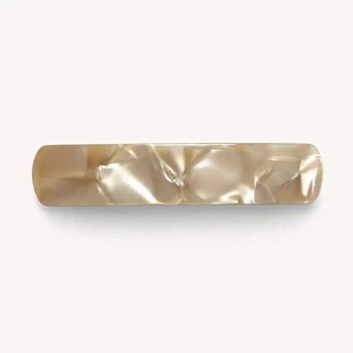 A MACHETE - NO. 3 HEIRLOOM BARRETTE IN SAND SHELL by MACHETE lies open on a white surface, revealing its clasp mechanism and gracefully curved shape. This handmade accessory features heirloom-quality craftsmanship in sand shell tones, ensuring durability as well as timeless elegance.