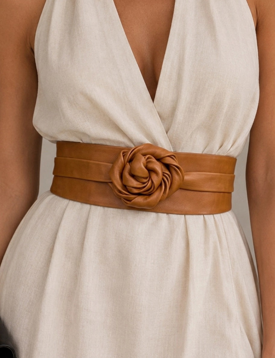 ADA - LEATHER WRAP BELT IN TOFFEE, a tan leather belt featuring a large rose-shaped accent at the center, worn over a cream-colored dress as a versatile one-size accessory.