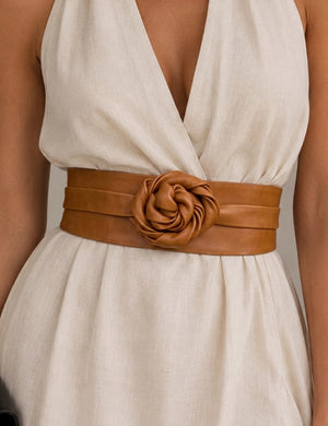ADA - LEATHER WRAP BELT IN TOFFEE, a tan leather belt featuring a large rose-shaped accent at the center, worn over a cream-colored dress as a versatile one-size accessory.