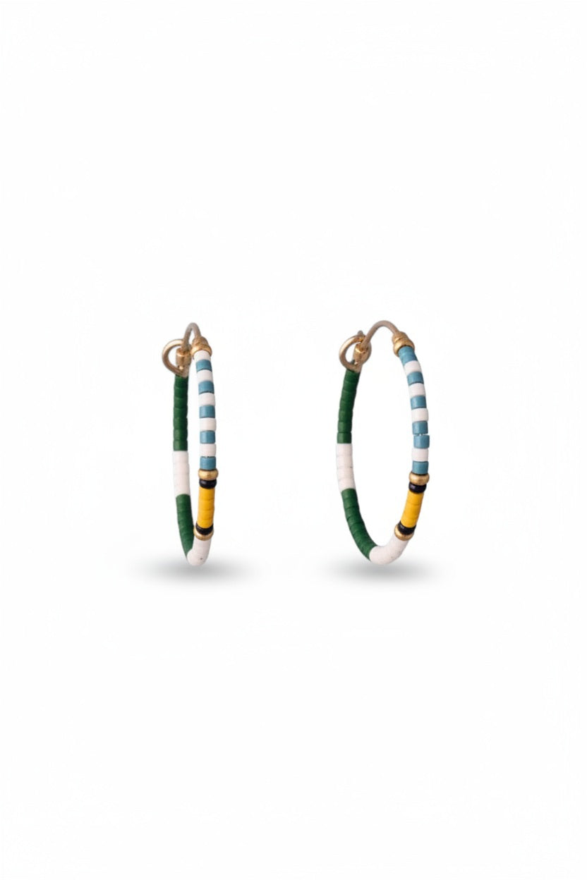 The ALICE RISE MIDI COLORLOOP EARRINGS IN FAIRWAY GREEN feature round 14k gold filled hoops with green, white, yellow, and black Japanese glass beads, displayed on a textured light blue background.