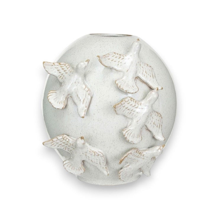 A wooden cabinet is adorned with VASE WITH BIRDS by CREATIVE COOP, handmade stoneware pieces showcasing intricate blue and white designs, complemented by assorted potted plants. The setup stands against a plain beige wall, enhancing the minimalist elegance of the decor.