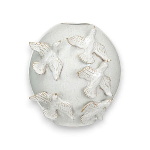 A wooden cabinet is adorned with VASE WITH BIRDS by CREATIVE COOP, handmade stoneware pieces showcasing intricate blue and white designs, complemented by assorted potted plants. The setup stands against a plain beige wall, enhancing the minimalist elegance of the decor.