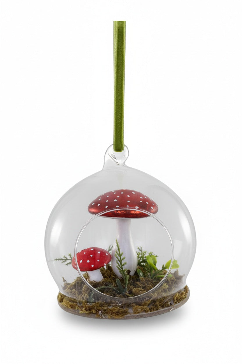 A 3.75-inch Cody Foster Woodland Mushroom Globe Ornament featuring two red and white spotted mushrooms on a bed of moss inside a glass globe, hanging from a green ribbon.