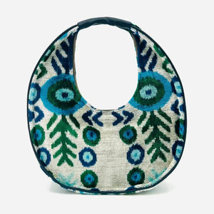 The BALDIZ LUCA BAG IN AQUA VINE is a circular handbag with a short handle, showcasing bold blue and green abstract shapes and leaves on a light background—perfect for everyday use and inspired by the signature style of BALDIZ.