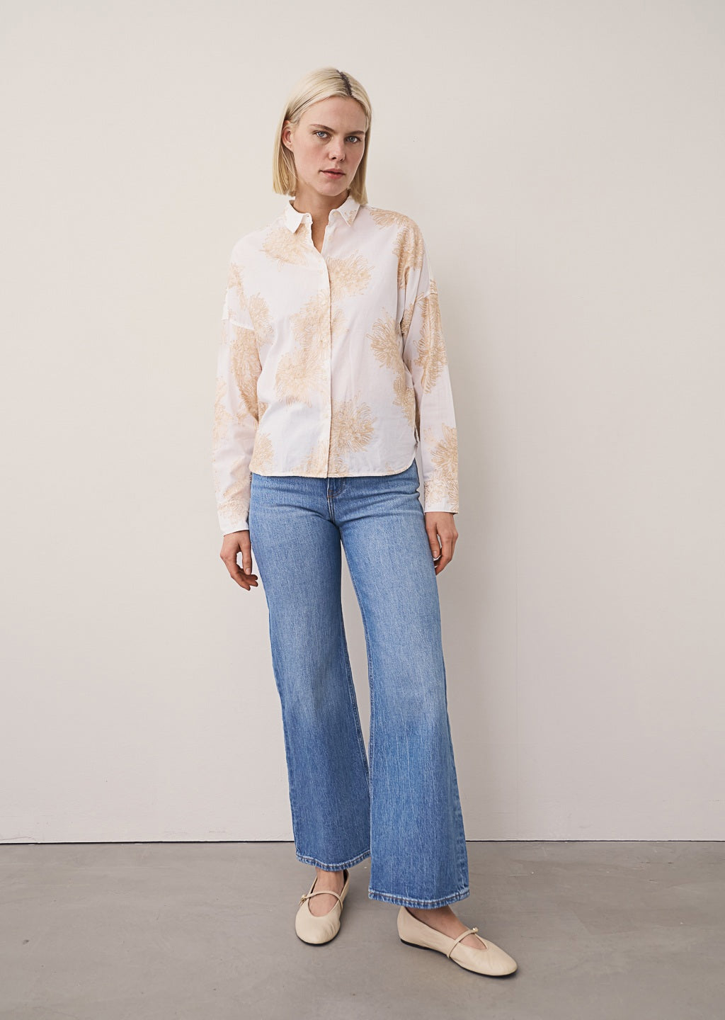 A close-up of the 0039 ITALY LUCY BLOUSE WITH EMBROIDERED FLOWERS, featuring detailed beige floral embroidery on pure cotton. A hand rests in the pocket, emphasizing the relaxed tailoring; the model’s face is out of frame.