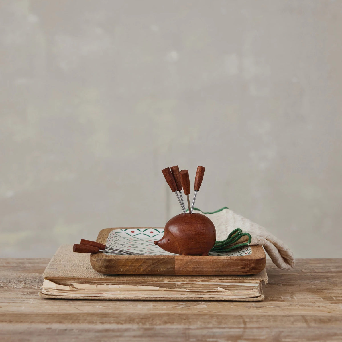 The CREATIVE COOP WOOD HEDGEHOG HOLDER WITH 6 APPETIZER PICKS features a charming wooden hedgehog design with small legs and a pointed nose, holding six metal picks in its back for a fun and functional table accessory.